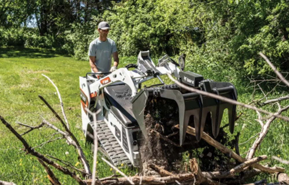 man operating a skid loader grabbing branches