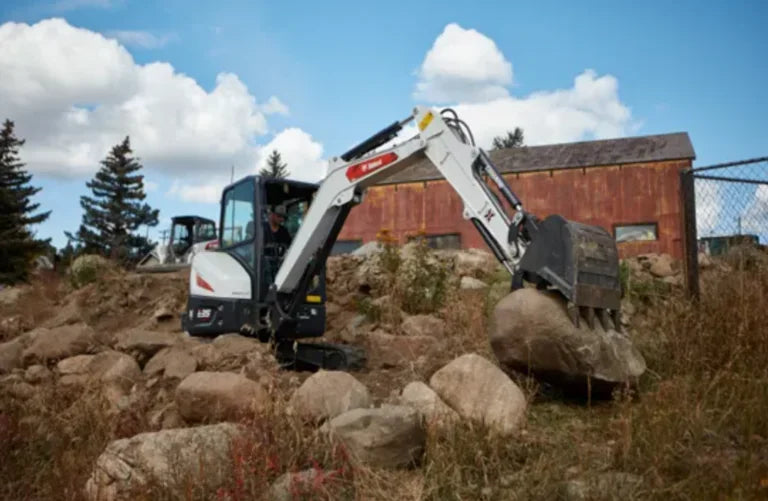 bobcat mini excavator moving large rocks in front of a barn