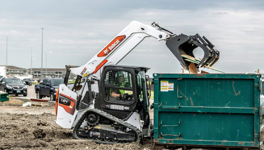 Bobcat dumping lumber into a dumpster