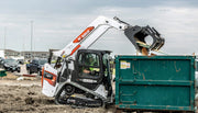 Bobcat dumping lumber into a dumpster